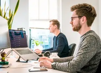 man sitting on chair wearing gray crew-neck long-sleeved shirt using Apple Magic Keyboard