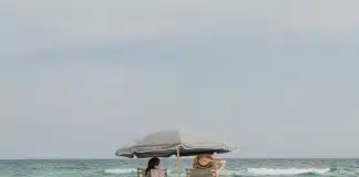 two people under beach umbrella near shoreline